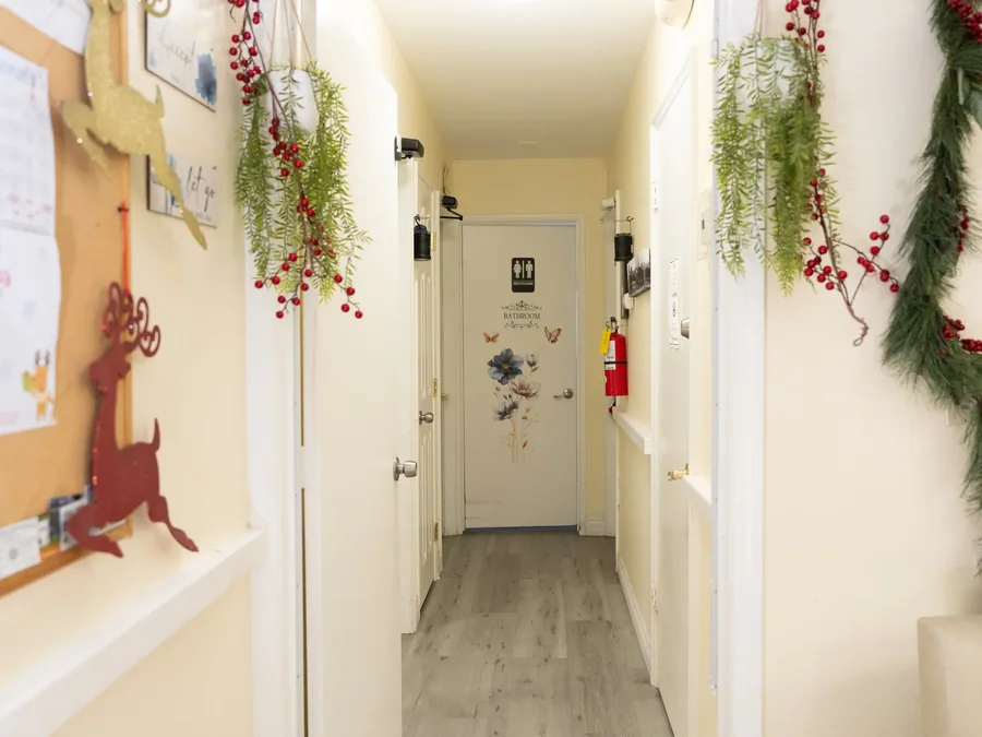 Bright hallway decorated with seasonal greenery and red berries leading to bathroom in residential care facility