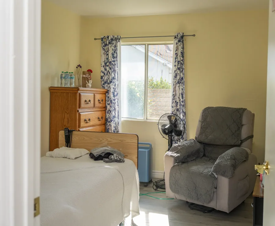 Bright residential care bedroom featuring hospital bed, comfortable recliner, and medical equipment with natural lighting